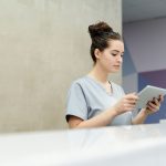 Profissional de recepção usando um tablet no balcão de uma clínica moderna.