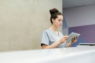 Profissional de recepção usando um tablet no balcão de uma clínica moderna.