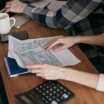 Mãos organizam formulários fiscais sobre uma mesa com calculadora, notebook e caderno.