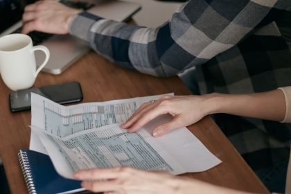 Mãos organizam formulários fiscais sobre uma mesa com calculadora, notebook e caderno.